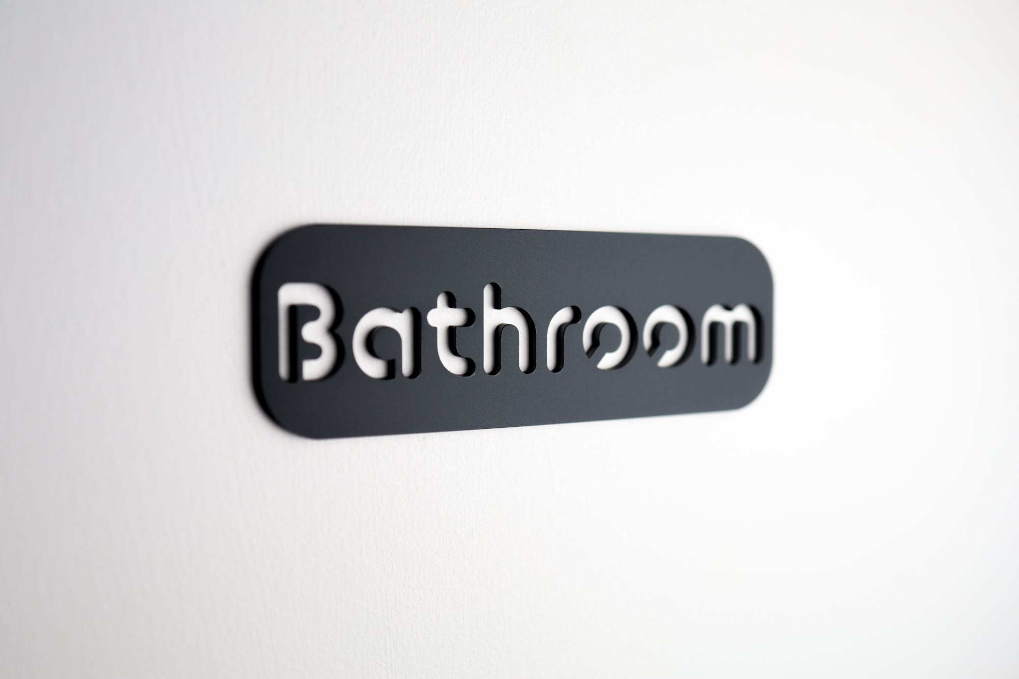 Black acrylic bathroom sign with "Bathroom" cut-out lettering on stone texture finish.